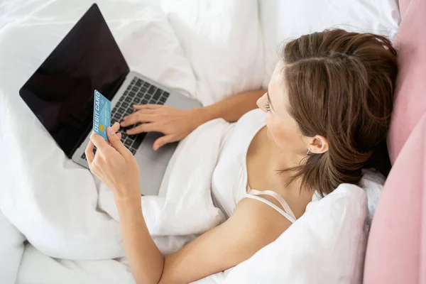 Menina com um cartão de débito deitado na cama — Fotografia de Stock