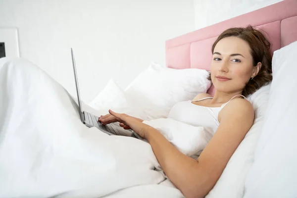 Sorrindo senhora digitando em seu laptop na cama — Fotografia de Stock