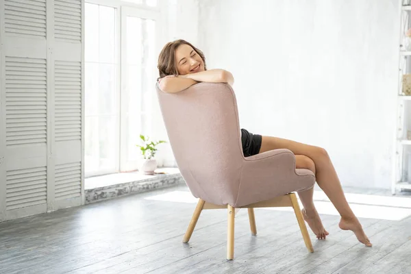 Glad kvinna sitter i en fåtölj hemma — Stockfoto