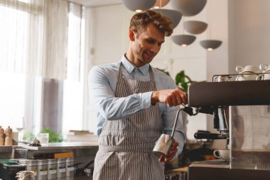 Profesyonel kahve makinesi kullanan önlüklü yakışıklı bir barmen.