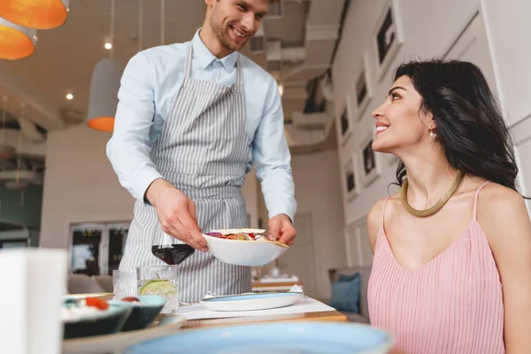 Vreugdevolle mannelijke ober serveert eten aan charmante dame — Stockfoto