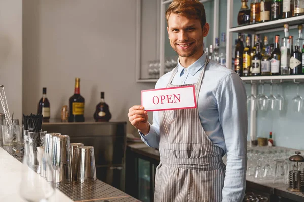 Veselý barman v zástěře drží otevřenou ceduli — Stock fotografie