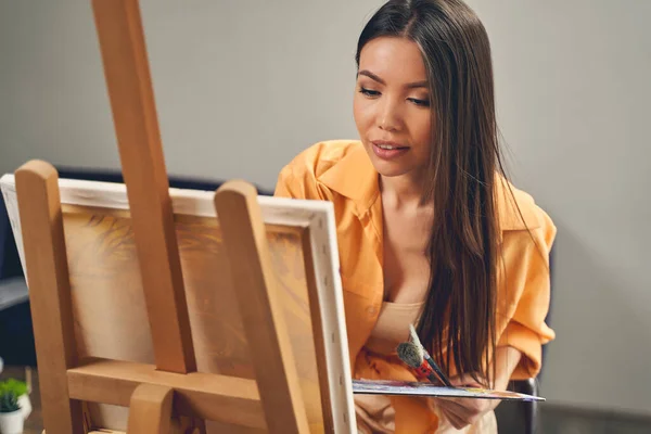 Encantadora jovem senhora pintura no cavalete em casa — Fotografia de Stock