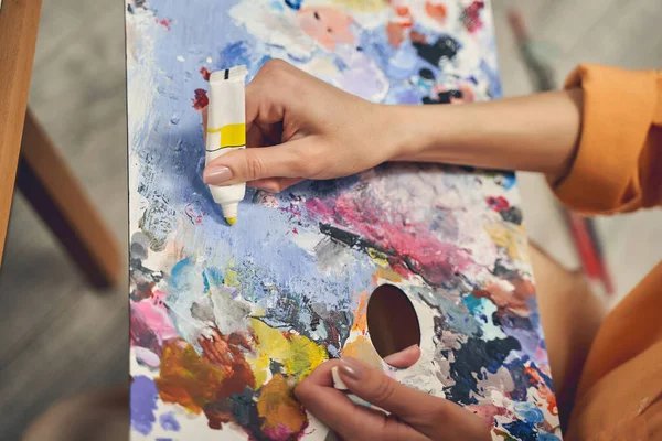 Young woman adding yellow paint to paint palette — Stock Photo, Image