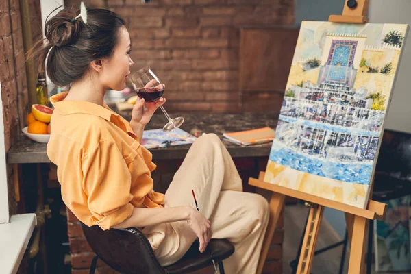 Urocza pani pijąca wino i patrząca na malowanie — Zdjęcie stockowe