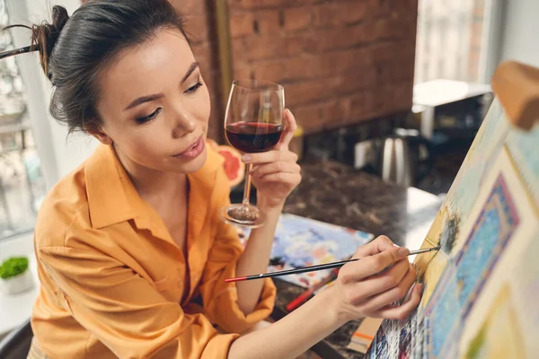 Schöne Dame trinkt Wein und malt auf Leinwand — Stockfoto