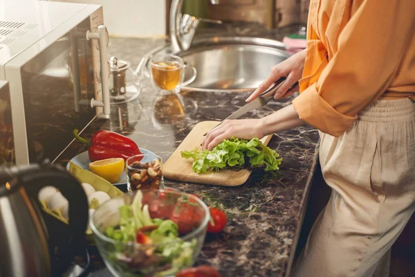 Молодая женщина руки режет салат ножом на кухне — стоковое фото
