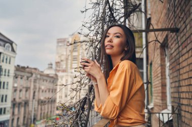 Genç ve güzel bir kadın balkonda şarap içiyor.