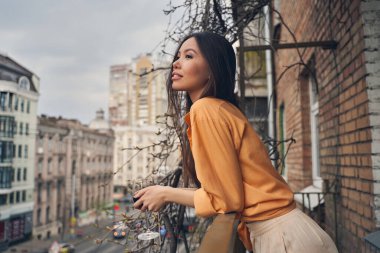 Güzel bayan balkonda dikiliyor ve şehre bakıyor.