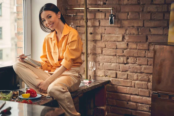 Jovem alegre sentada na bancada da cozinha — Fotografia de Stock