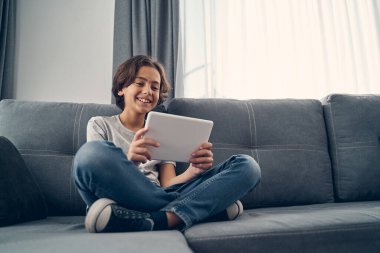 Küçük çocuk kanepede oturuyor ve bacak bacak üstüne atıyor.