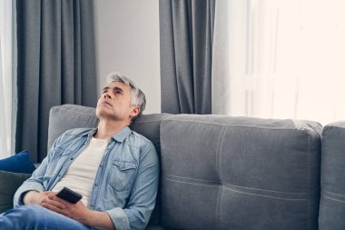 Kot pantolon ve gömlek giyen adam üzgün görünüyor.