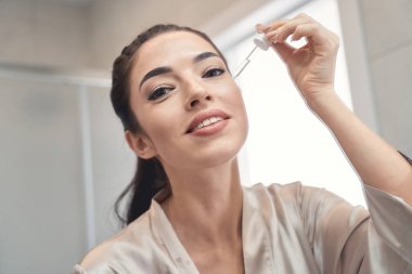 Güzel genç bayan banyoda göz emülsiyonu uyguluyor.