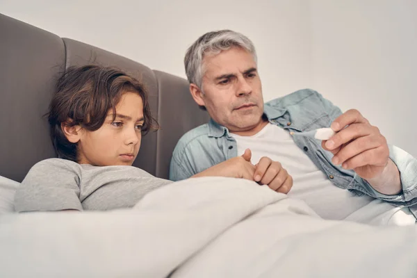 Blanke man liggend in bed met zieke zoon — Stockfoto