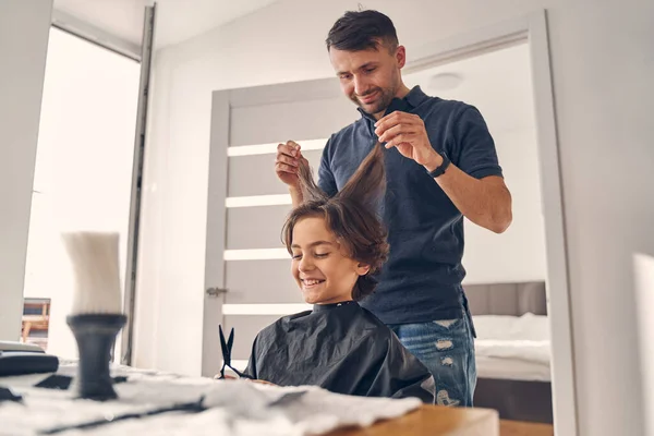 Cabeleireiro jovem atraente mudando penteado da criança — Fotografia de Stock