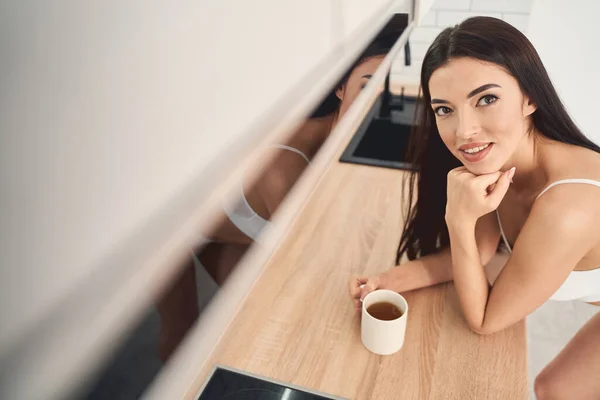 Портрет молодой очаровательной леди с чашкой чая за кухонным столом — стоковое фото