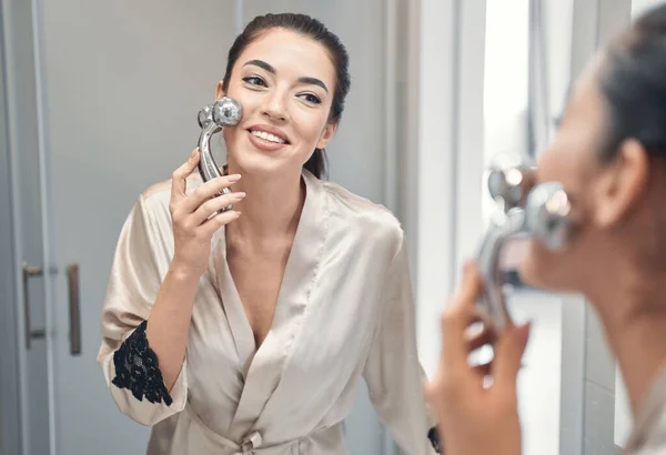 Mujer bastante joven en un albornoz haciendo procedimientos de masaje para la cara —  Fotos de Stock