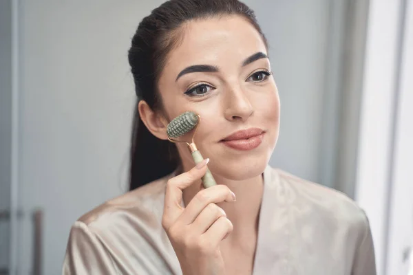 Charming young lady doing face care massage and using roller — Stock Photo, Image