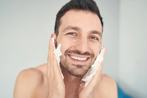 Joven alegre se pone jabón de afeitar en las mejillas — Foto de Stock