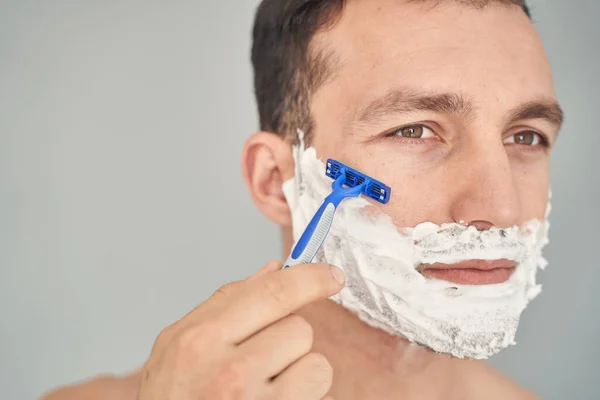 Concentrated young man shaving his face in the morning — Stock Photo, Image