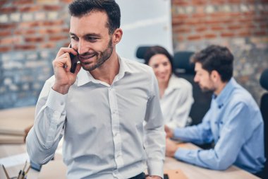 Ofiste akıllı telefonla konuşan gülümseyen işadamı.