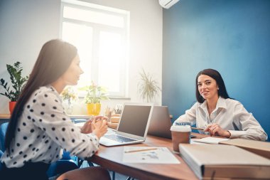 Mutlu bayan iş arkadaşları güneşli bir günde ofiste oturuyorlar.