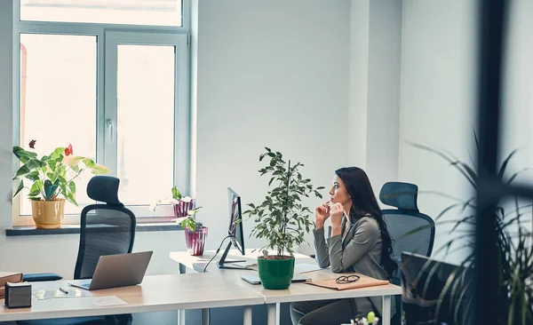 Kvinna tittar på fönstret och sitter vid skrivbordet med dator — Stockfoto