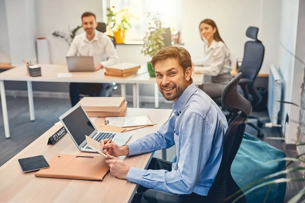 Sorrindo homem está segurando notebook no local de trabalho — Fotografia de Stock