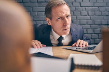 Ciddi bir ofis çalışanı dizüstü bilgisayarının önünde oturuyor.