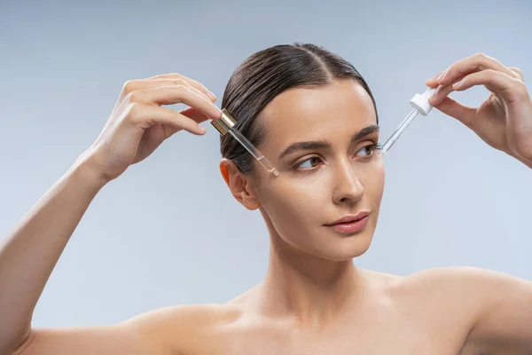 Young woman applying cosmetic oil on skin — Stock Photo, Image