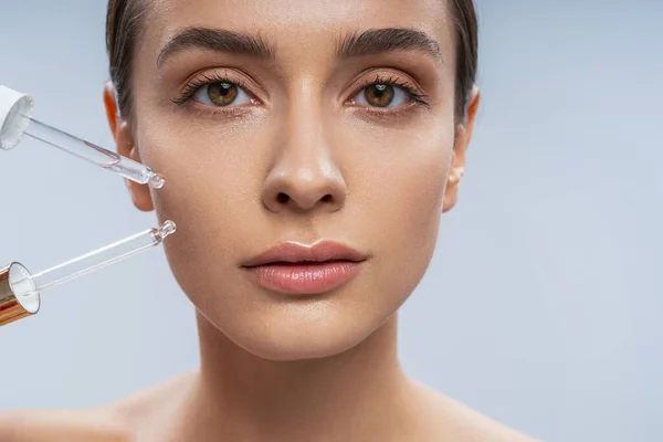 Jovem bela mulher aplicando óleo facial na bochecha — Fotografia de Stock