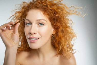 Gülümseyen kırmızı kadın kaşlarına bakıyor.