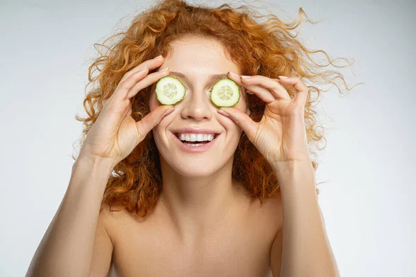 Merry red woman with cucumber slices on eyes — Stock Photo, Image