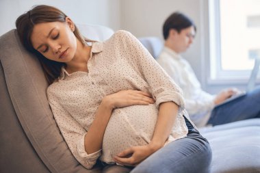 Evdeki kanepede uykulu görünen hamile bir kadın.