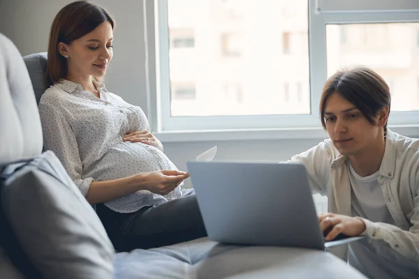 Unga par hemma under graviditeten på soffan vid fönstret — Stockfoto