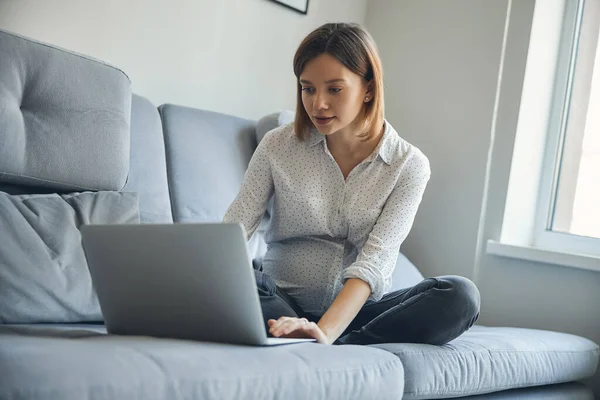 Joven embarazada con dispositivo moderno en el sofá — Foto de Stock