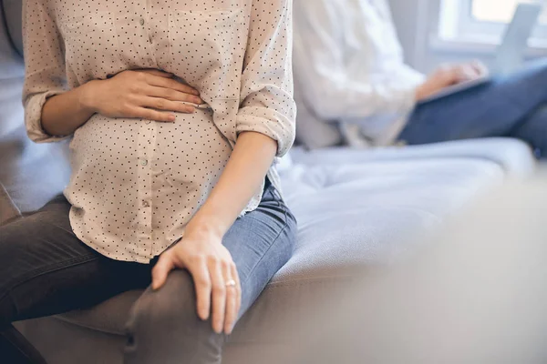 Жінка в сорочці і джинсах торкається її вагітного живота — стокове фото