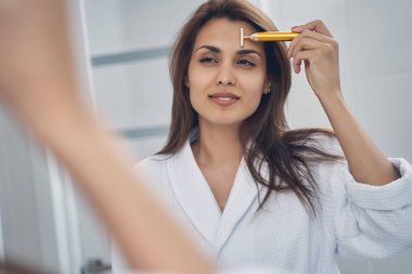 Çekici bir genç kadın altın yüz masajı aleti kullanıyor.