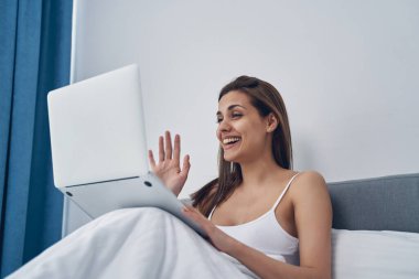 Neşeli genç bir kadın video aracılığıyla arkadaşlarıyla sohbet ediyor.