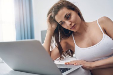 Yatak odasında dizüstü bilgisayar kullanan güzel bir genç kadın.