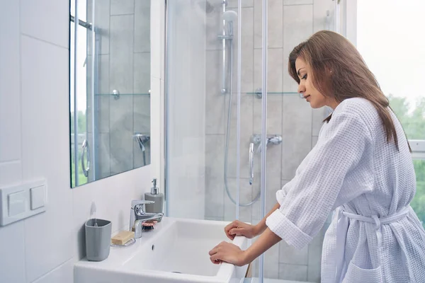 Beautiful young woman standing by the sink in bathroom — Stock Photo, Image