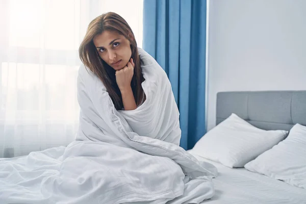 Mujer joven trastornada sentada en la cama en el dormitorio —  Fotos de Stock