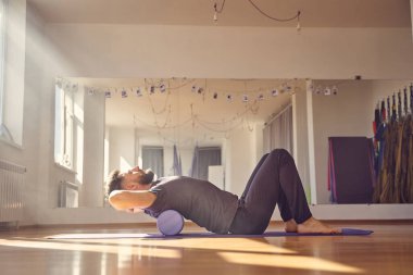 Atletik genç adam köpük silindirle egzersiz yapıyor.