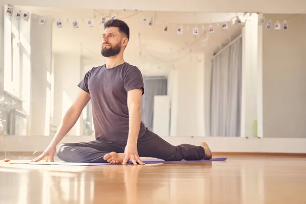 Atletisk ung man gör duva poserar i yoga studio — Stockfoto