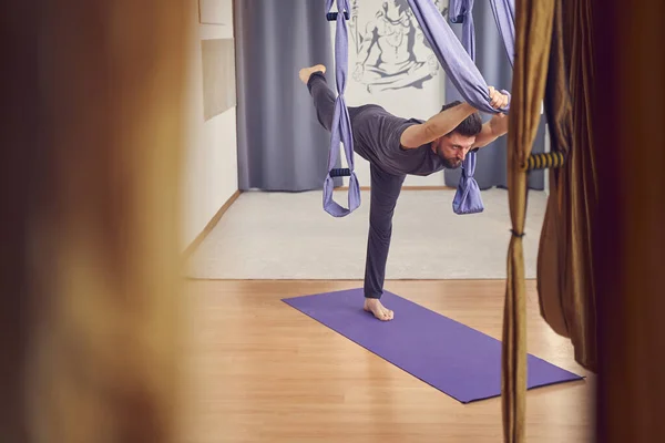 Sportlicher junger Mann praktiziert Antigravitations-Yoga im Studio — Stockfoto