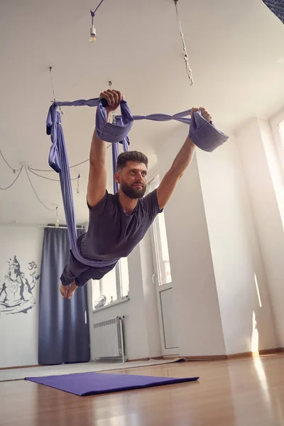 Schöner junger Mann praktiziert Antigravitations-Yoga im Studio — Stockfoto