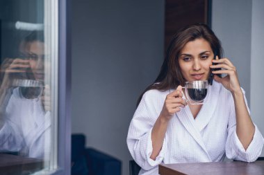 Çay içen ve cep telefonuyla konuşan çekici genç bir kadın.