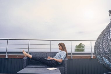 Çatıdaki terasta dizüstü bilgisayarda çalışan güzel genç bir kadın.