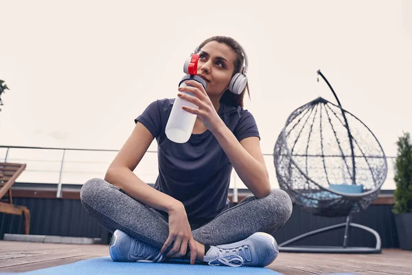 Encantadora deportista con auriculares bebiendo agua y escuchando música — Foto de Stock