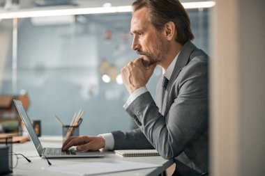 Parlak ofiste bilgisayarla çalışan yetişkin bir adam.